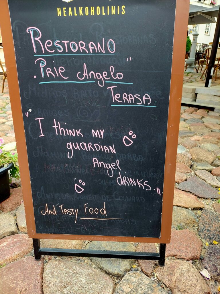 Lavagna fuori da un bar in cui è scritto "penso che il mio angelo custode beva"