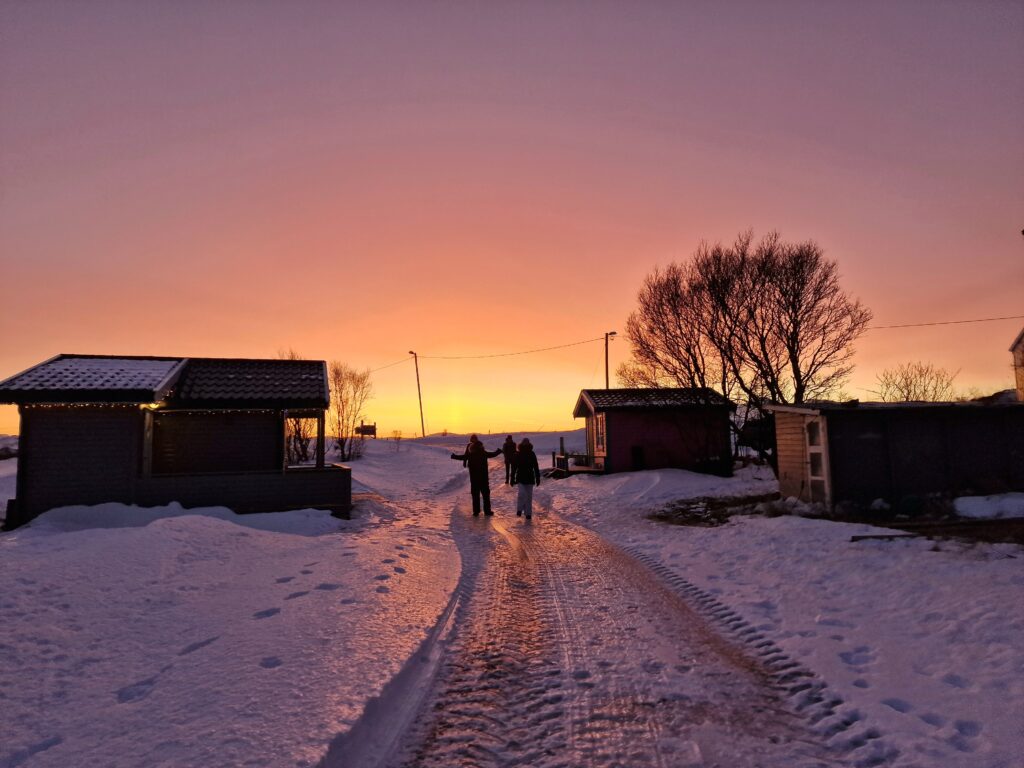 Persone che camminano su strada innevata con cielo rosa e giallo, durante la notte polare finalndese.