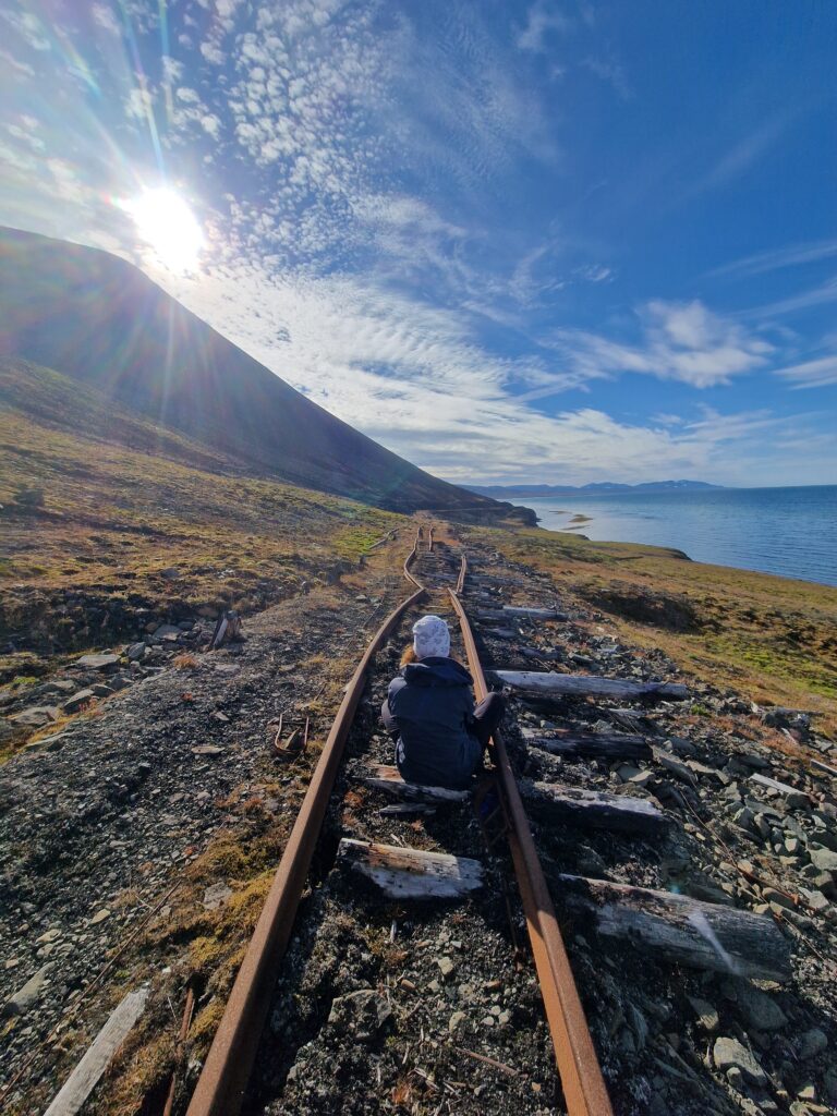Persona di spalle seduta sui binari di una ferrovia abbandonata, in riva al mare